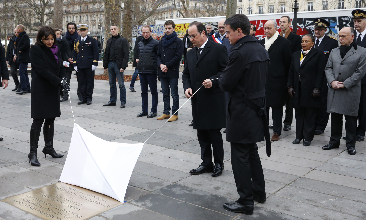 French President Francois Hollande (C), Prime Minister Manuel Valls (R) and Paris Mayor Anne Hidalgo (L) unveil a commemorative plaque during a ceremony held, on January 10, 2016 to mark a year since 1.6 million people thronged the French capital in a show of unity after attacks on the Charlie Hebdo newspaper and a Jewish supermarket. Just as it was last year, the vast Place de la Republique will be the focus of the gathering as people reiterate their support for freedom of expression and remember the other victims of what would become a year of jihadist outrages in France, culminating in the November 13 coordinated shootings and suicide bombings that killed 130 people and were claimed by the Islamic State (IS) group. / AFP / POOL / PHILIPPE WOJAZER