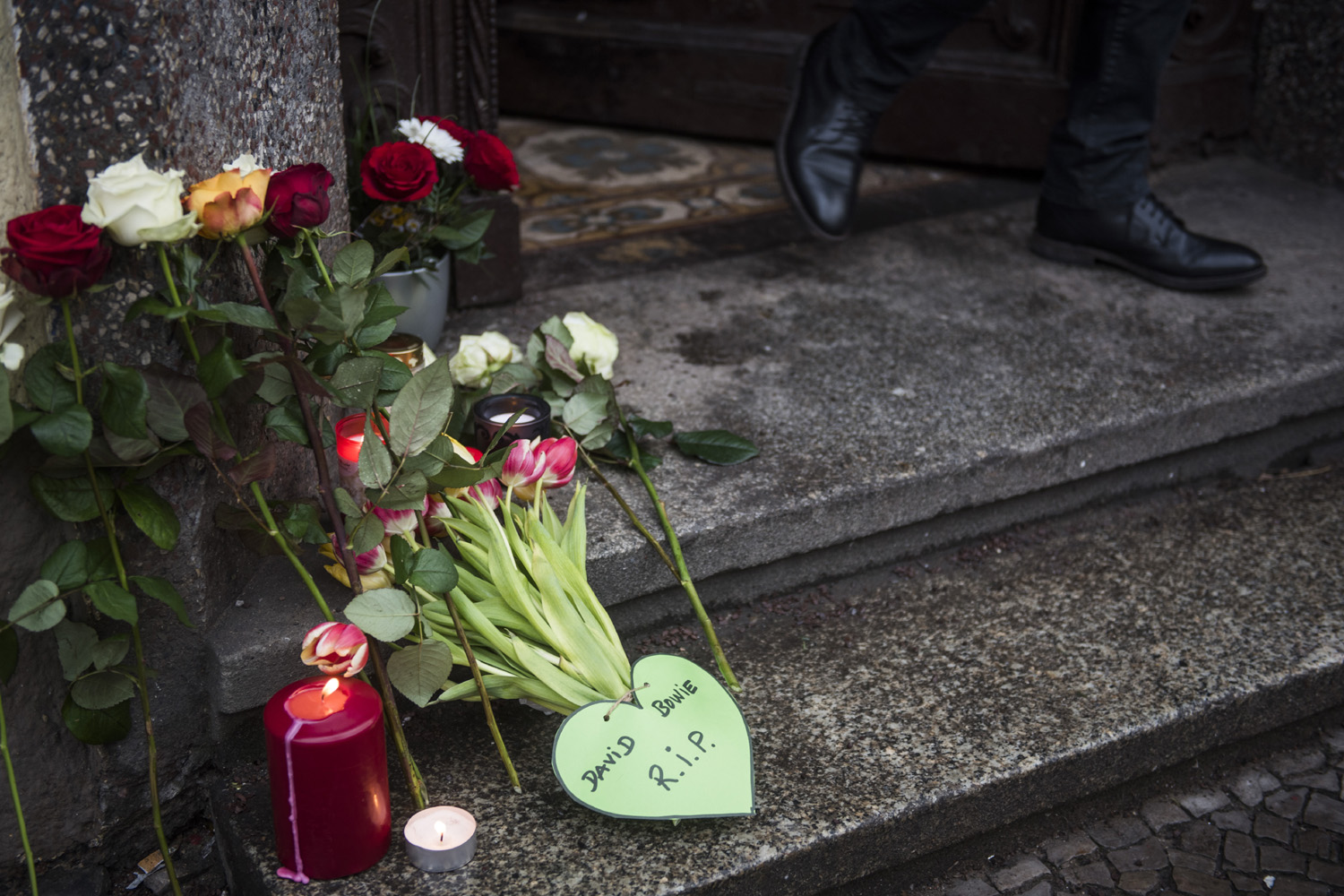A resident leaves the building among tributes to British rock legend David Bowie leftoutside his former home in Berlin's Hauptstrasse 155 on January 11, 2016. British rock music legend David Bowie has died after a long battle with cancer, his official Twitter and Facebook accounts said. / AFP / ODD ANDERSEN