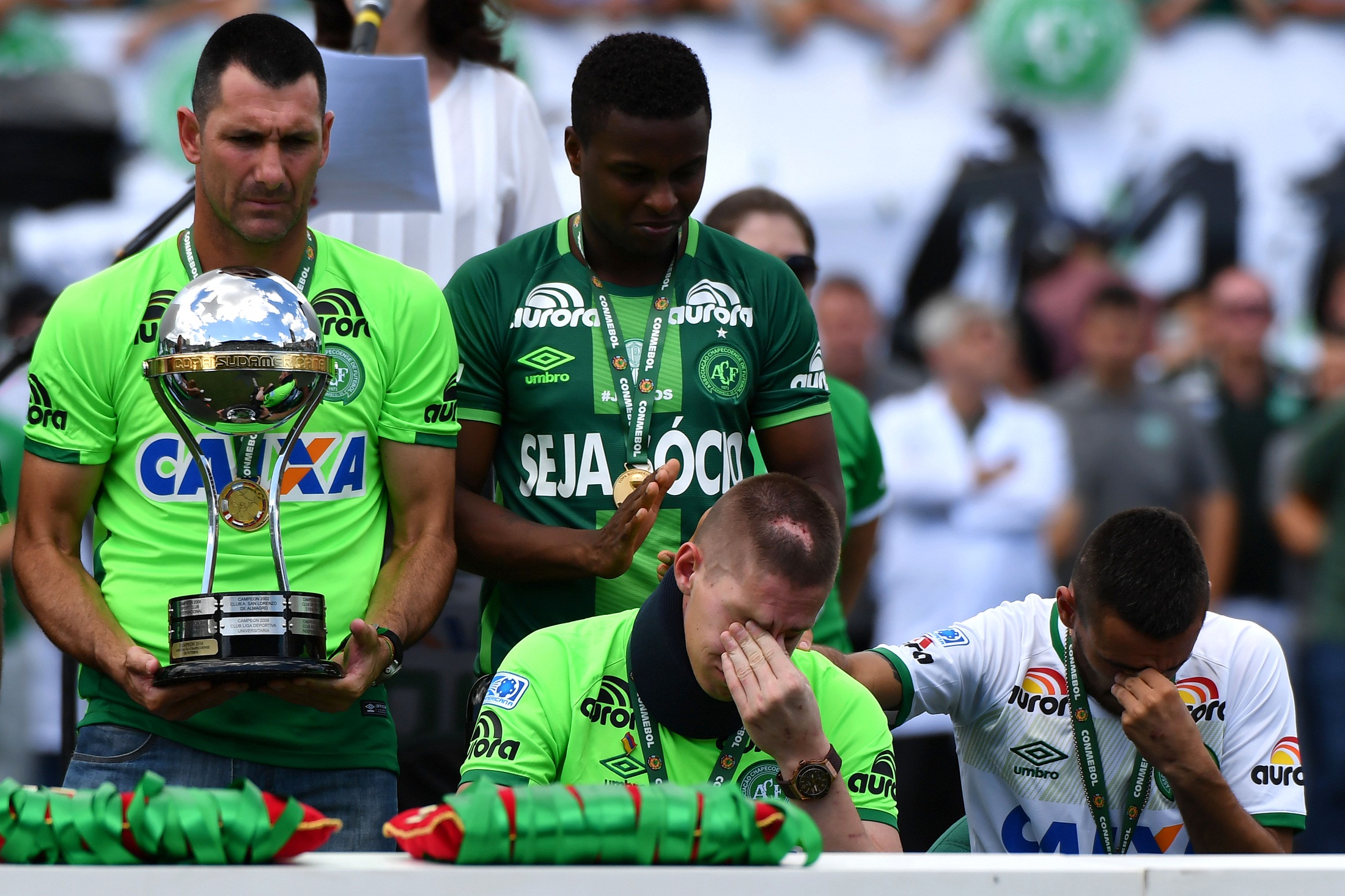 Brazilian Chapecoense footballers Alan Ruschel (R) and Jackson Follmann (C), survivors of the LaMia airplane crash in Colombia, receive the Copa Sudamericana trophy at the Arena Conda stadium in Chapeco, Santa Catarina state, in southern Brazil on January 21, 2017, before a friendly match against Palmeiras - Brazilian Champion 2016.  Most of the members of the Chapocoense football team perished in a November 28, 2016 plane crash in Colombia. / AFP PHOTO / NELSON ALMEIDA